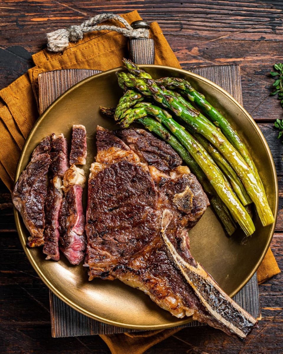 A bone-in ribeye carved and served with grilled asparagus