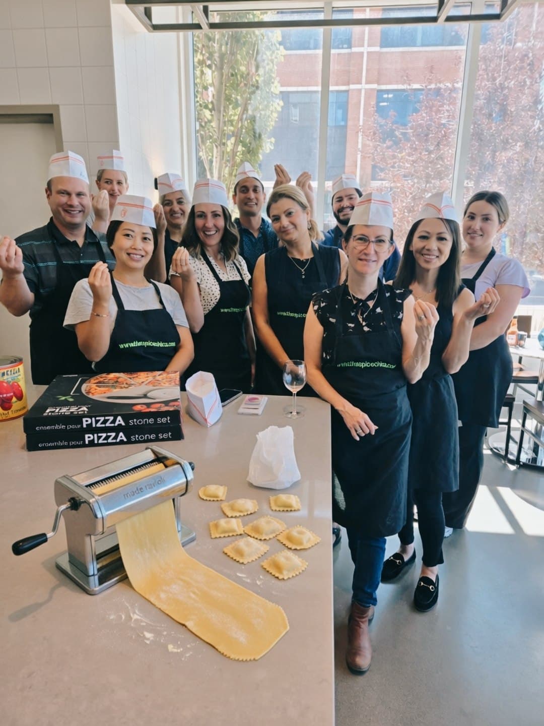 A team in chef hats and aprons gathered around fresh pasta and ravioli during a hands-on cooking class with Chef Marina